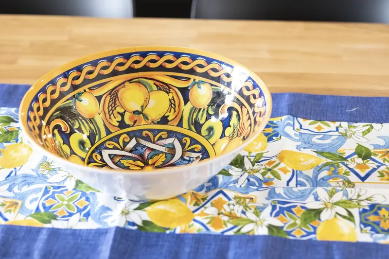 A hand-painted Sicilian ceramic bowl with lemons on a patterned runner