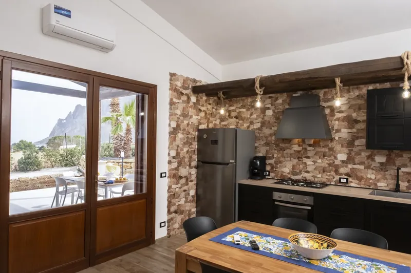 Kitchen with an exposed stone wall, black units and a wooden dining table