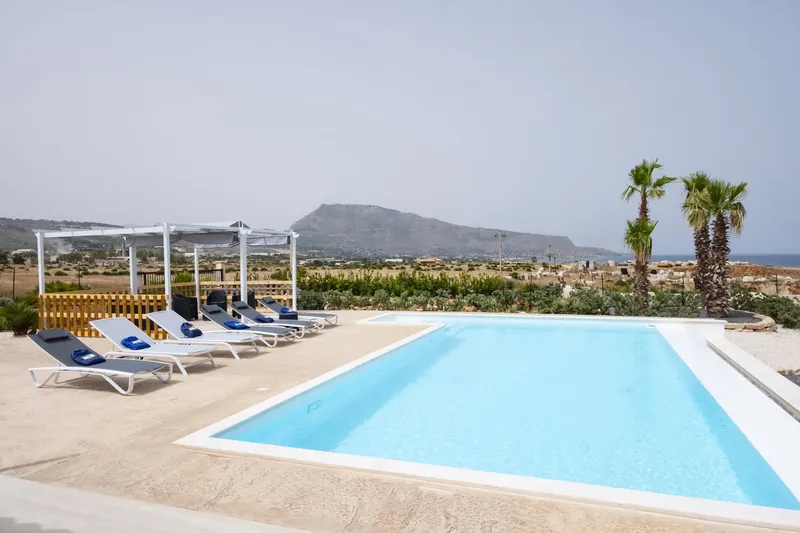 The private pool with sun loungers, palms, Monte Cofano and the open sea